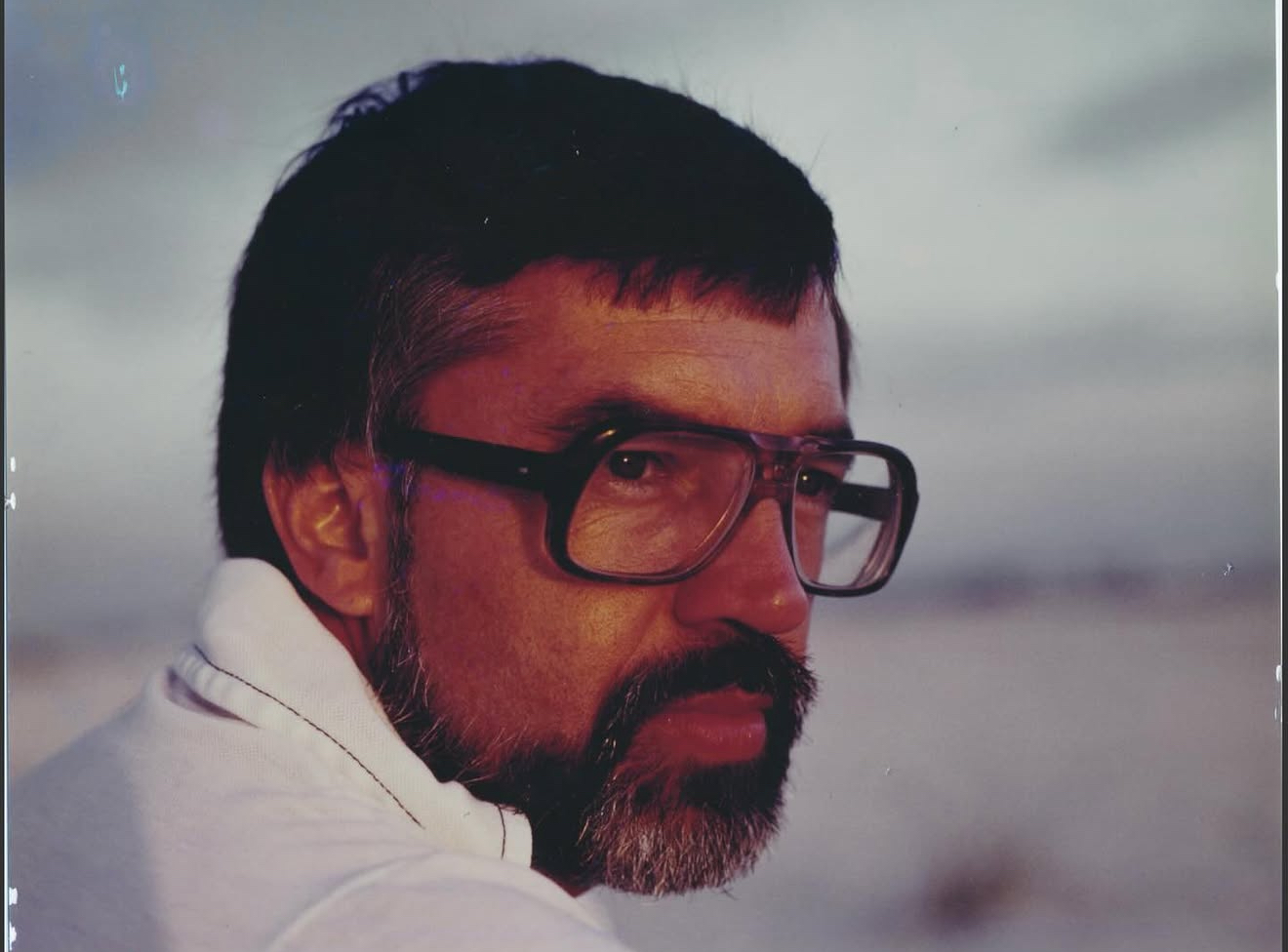 Vintage color portrait of former department head Charles Groover, a man with dark hair, glasses and a beard, against a blurred outdoor background.