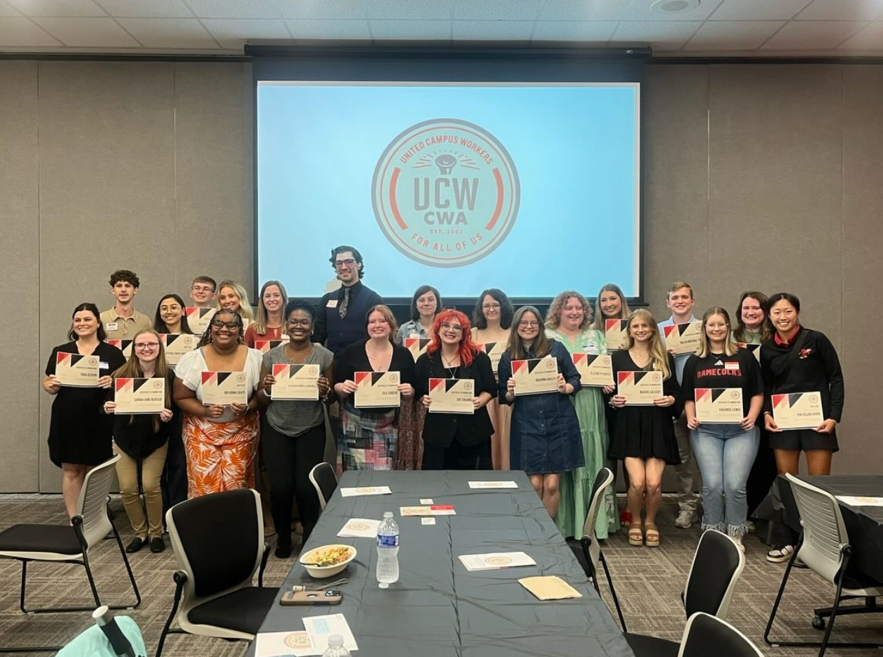 Group of student award nominees holding certificates in front of a screen reading "United Campus Workers, CWA, for all of us," for the JSU Student Worker of the Year Award.