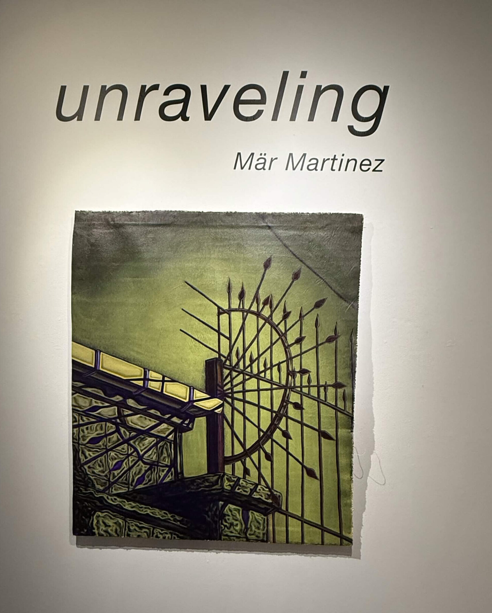 Gallery wall reading "unraveling, Mar Martinez" above a textile print artwork showing an ornate wrought iron gate against a green background.